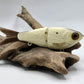 A small, realistic looking fishing lure with bone coloring, attached to a hook, resting on a wooden surface.