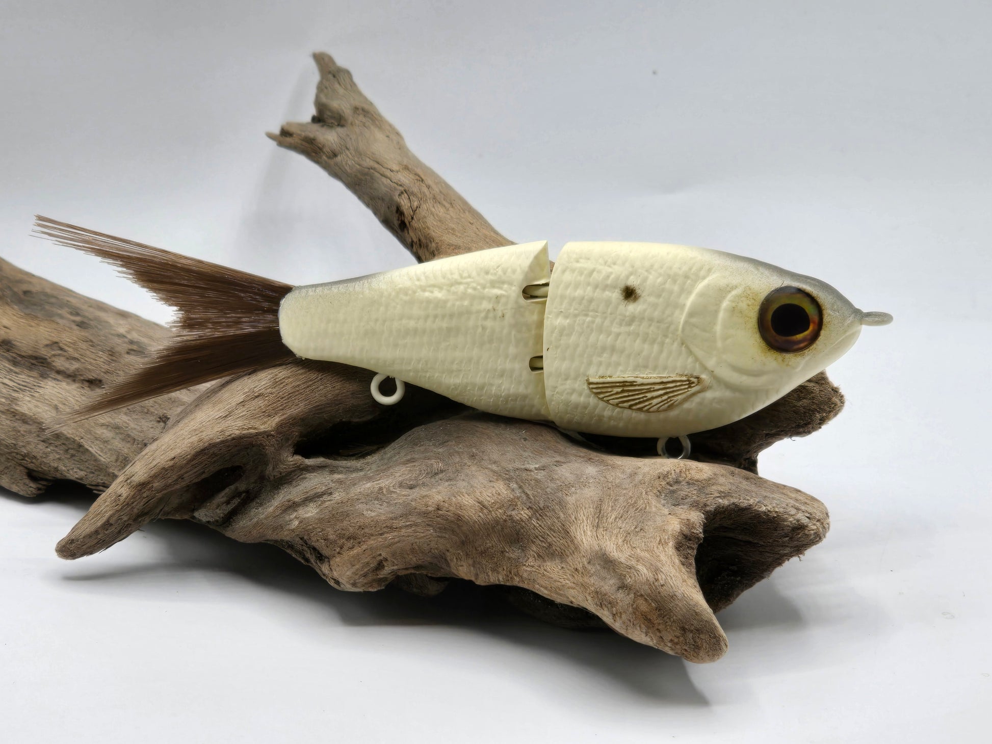 A small, realistic looking fishing lure with bone coloring, attached to a hook, resting on a wooden surface.